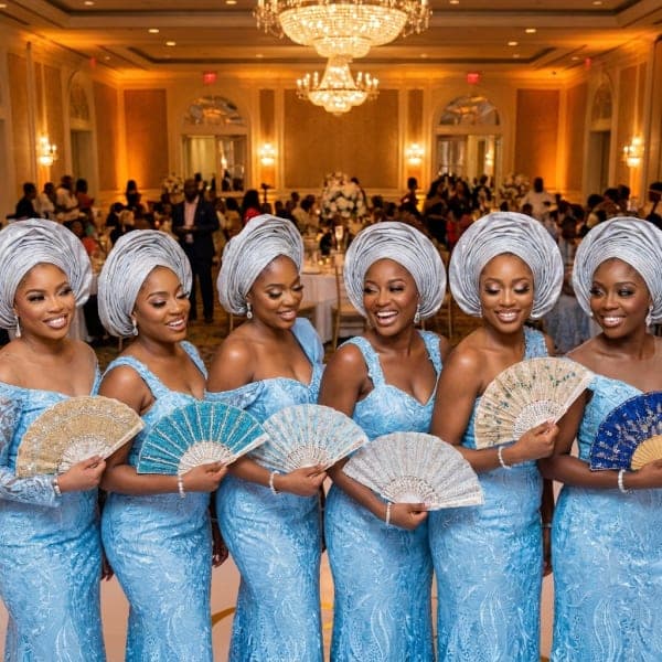Aso-ebi party in matching blue lace and silver gele holding hand fans